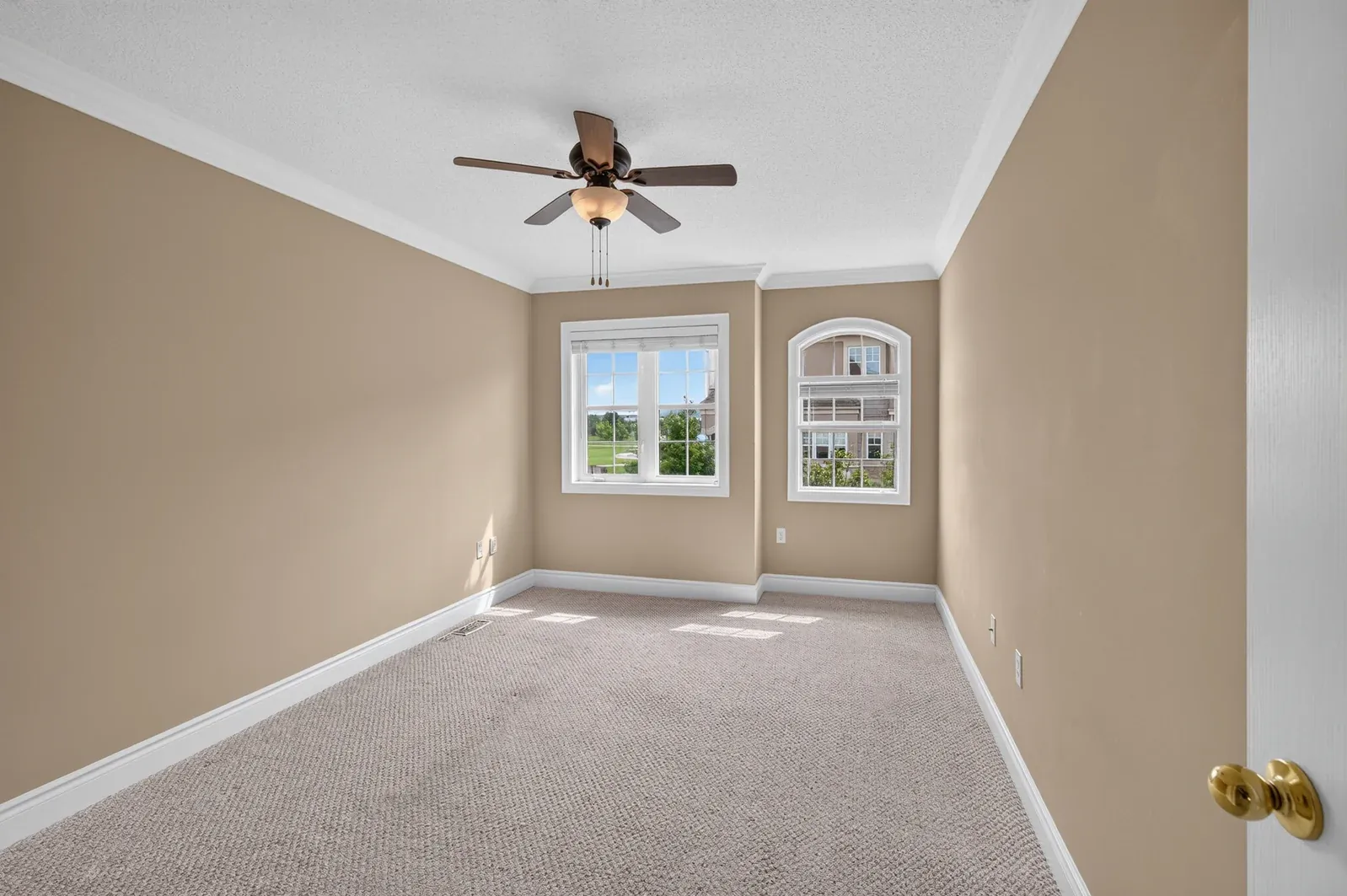 Empty bedroom with beige walls, carpet, a ceiling fan and two windows, before virtual staging