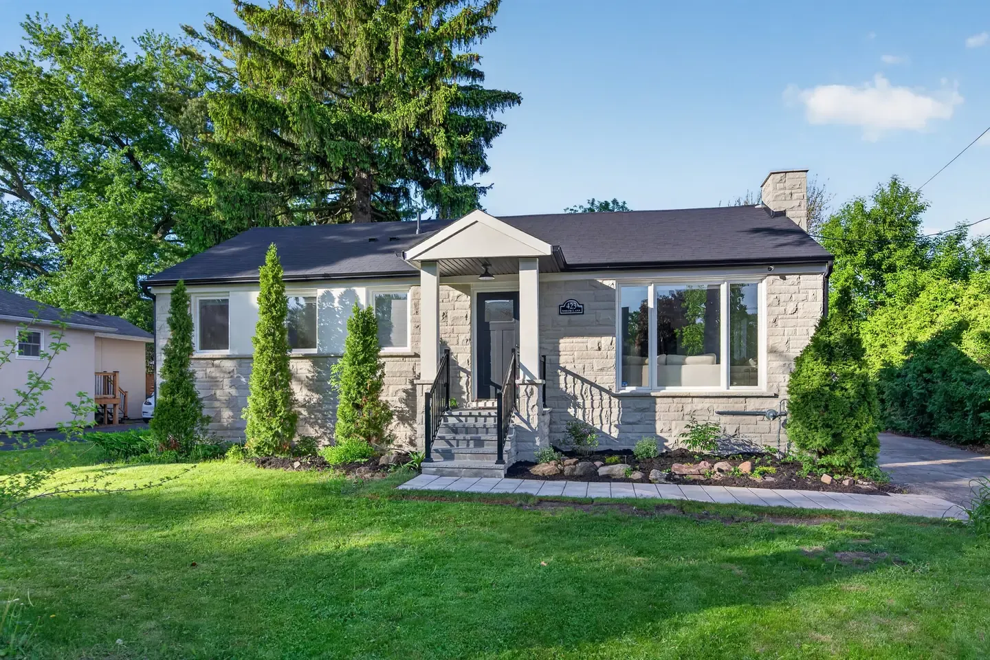 Daytime exterior of a stone bungalow with a front lawn and blue sky, before the AI dusk edit